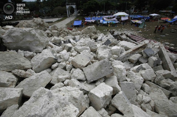 Residents stay in makeshift shelters in front of a heap of rubble from the collapsed Our Lady of Light church in Loon