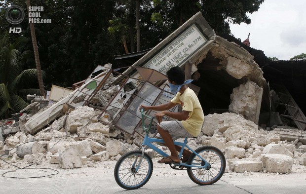A boy rides a bicycle past a destroyed building in Loon, Bohol a day after an earthquake hit central Philippines