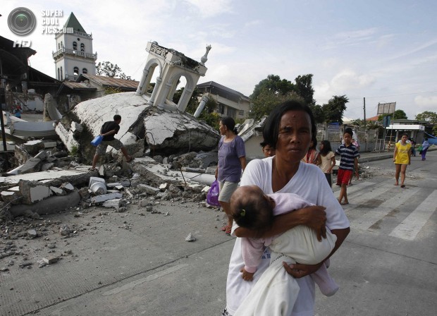 A woman carries her baby past a destroyed church belfry in Tubigon